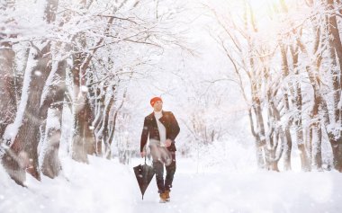 Parkta yürüyen bir adam. Kışın kar altında şemsiyeli genç bir adam..