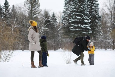 Mutlu bir aile kışın dışarıda karda oynar ve güler. Şehir parkı kış günü.