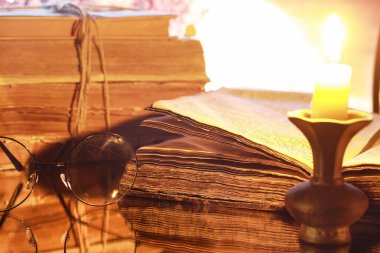 Ay 'ın arka planında eski bir retro kitapta antika gözlükler. Mum ışığından kitap okuyor. Kitap gerilim ve roman konsepti..