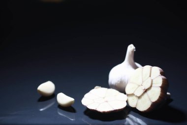 Siyah arka planda taze sarımsaklı karanfil. Sarımsak vitamin açısından zengindir, kullanışlı bahar, iyi baharatlar. Karanlık bir arka planda dilimlenmiş sarımsak. Çiğ sarımsak..