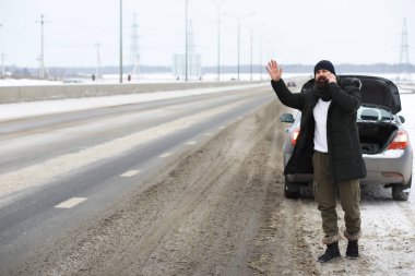 Kış yolunda kırık arabanın yanında duran sakallı adam.