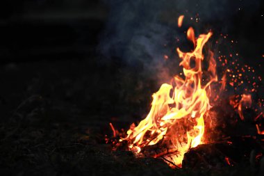 Büyük ateşte yanan kızıl kıvılcımlar uçuşur. Yanan kömürler, yanan parçacıklar siyah arkaplanda uçuşuyor..
