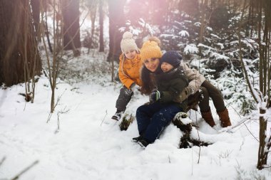 Mutlu bir aile kışın dışarıda karda oynar ve güler. Şehir parkı kış günü.