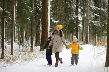 Mutlu bir aile kışın dışarıda karda oynar ve güler. Şehir parkı kış günü.