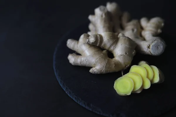 Ginger root whole and sliced. Ginger tea with lemon on the dark background. Fresh ginger root on stone background. Vitamins. Top view. Free space for your text.