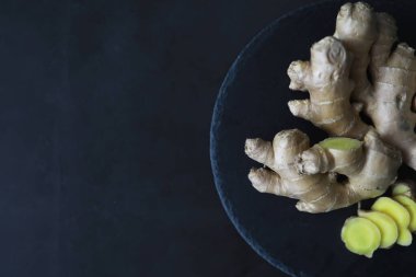 Zencefil kökü bütün ve dilimlenmiş. Koyu arkaplanda limonlu zencefil çayı. Taş zeminde taze zencefil kökü. Vitaminler. Üst Manzara. Metnin için boş yer.