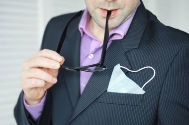 Tek kullanımlık bir tıbbi maske peçeteden sarkıyor. Takım elbiseli ve kot pantolonlu tek kullanımlık maskeli bir adam. Bireysel solunum koruması.