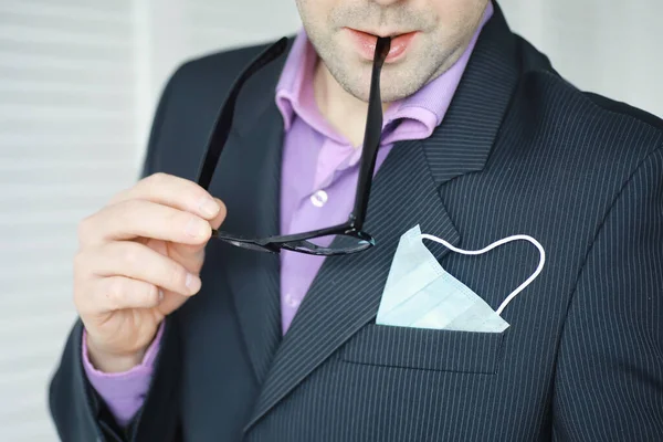 Tek kullanımlık bir tıbbi maske peçeteden sarkıyor. Takım elbiseli ve kot pantolonlu tek kullanımlık maskeli bir adam. Bireysel solunum koruması.