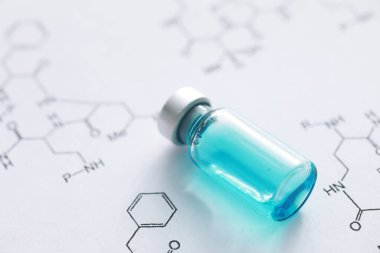 Kimyasal formülün yanındaki mavi arka planda enjeksiyon için küçük kavanozlar ve şırıngalar.