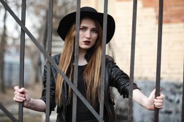 Şapkalı ve dışarıda siyah makyajlı güzel bir kız. Sokakta Gotik tarzında bir kız. Şehir caddesinde bir kız yürüyor. Deri yelekli ve telefonlu.