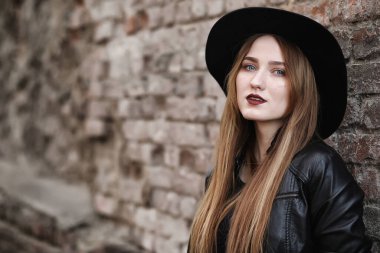 Şapkalı ve dışarıda siyah makyajlı güzel bir kız. Sokakta Gotik tarzında bir kız. Şehir caddesinde bir kız yürüyor. Deri yelekli ve telefonlu.