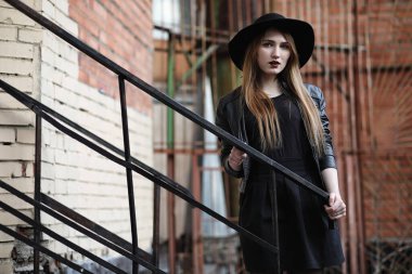 Şapkalı ve dışarıda siyah makyajlı güzel bir kız. Sokakta Gotik tarzında bir kız. Şehir caddesinde bir kız yürüyor. Deri yelekli ve telefonlu.
