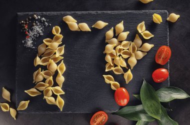 Siyah taş üzerine makarna kabukları. Domates ve defne yaprağı baharat ve deniz tuzu ve sarımsak ile.