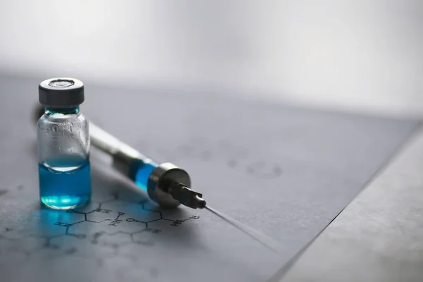 small jars with injection and syringe for injection on blue background near the chemical formul