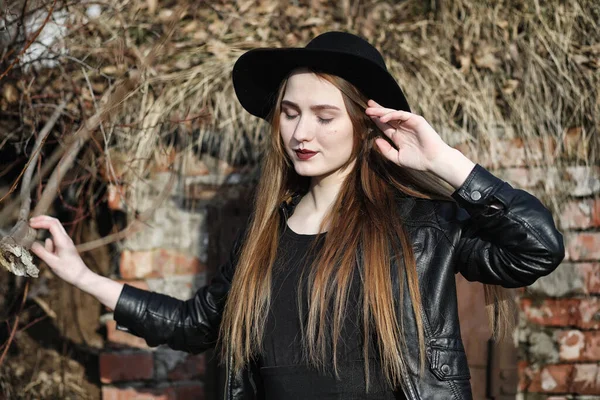 Şapkalı ve dışarıda siyah makyajlı güzel bir kız. Sokakta Gotik tarzında bir kız. Şehir caddesinde bir kız yürüyor. Deri yelekli ve telefonlu.