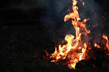 Büyük ateşte yanan kızıl kıvılcımlar uçuşur. Yanan kömürler, yanan parçacıklar siyah arkaplanda uçuşuyor..
