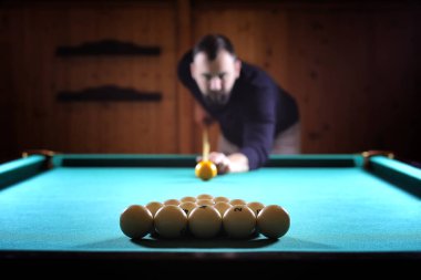 Sakallı bir adam büyük bir bilardo oynar. 3,5 metrelik havuzda parti. Kulüp oyununda erkekler için bilardo. Elinde ıstakayla bir adam piramidi kırar.