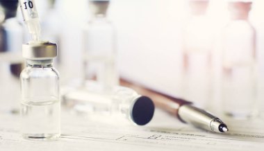 Bir adam tıbbi belge imzalıyor. Tıbbi ekipmanlar masada. Stetoskop ve şırıngalı ampuller. Ofiste notlar alıyor. Tıp Merkezi.