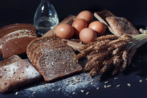 Fresh loaves of bread with wheat and gluten on a black table. Bakery and grocery concept. Fresh, healthy sorts of rye and white loaves, sprinkled flour on sackcloth food closeup. Fresh homemade bread with cereals.