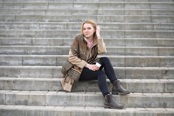 Şehirdeki sevimli sarışın merdivenlerde kahve içiyor.