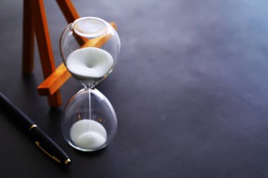 Kum saati ampulleri arasında koşan ve bir geri sayım bitiş tarihine kadar geçen zamanı ölçen, fotokopi alanı olan karanlık bir zemin arka planında..