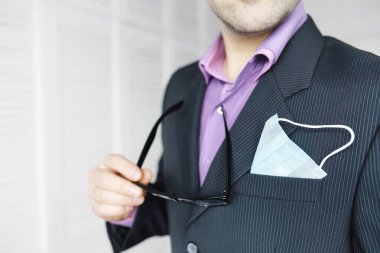 Tek kullanımlık bir tıbbi maske peçeteden sarkıyor. Takım elbiseli ve kot pantolonlu tek kullanımlık maskeli bir adam. Bireysel solunum koruması.