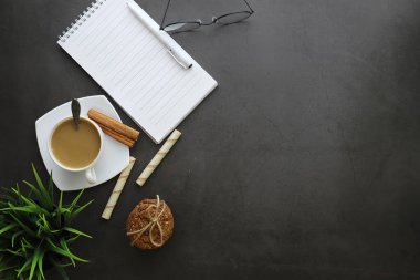Ofis masaüstü arka planında bir fincan kahve ve yazma aletleri var. Müdürün masası, kalemi, defteri..