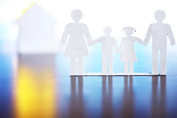 Cutout paper chain family with the protection of cupped hands, concept for security and care. Hands with cut out paper silhouette on table. Family care concept