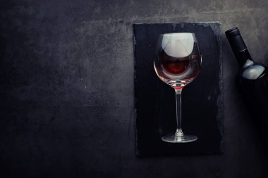 Taş zeminde kırmızı şarap. Şarap kadehi ve siyah şarap şişesi. Fındık peynir ve domates snack için.
