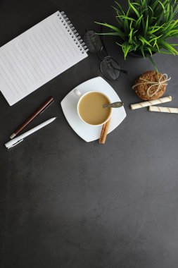 Ofis masaüstü arka planında bir fincan kahve ve yazma aletleri var. Müdürün masası, kalemi, defteri..