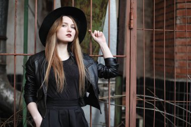 Şapkalı ve dışarıda siyah makyajlı güzel bir kız. Sokakta Gotik tarzında bir kız. Şehir caddesinde bir kız yürüyor. Deri yelekli ve telefonlu.