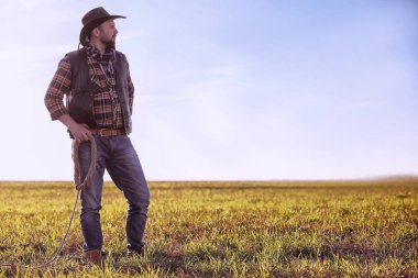 Şapkalı bir kovboy ve güneş altında bir tarlada duran bir kementle.