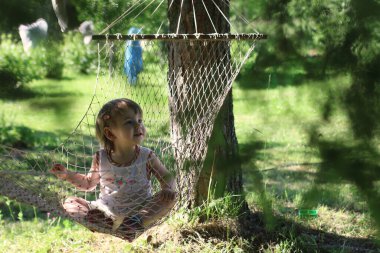 Çocuk güneşli bir günde hamakta oturuyor.