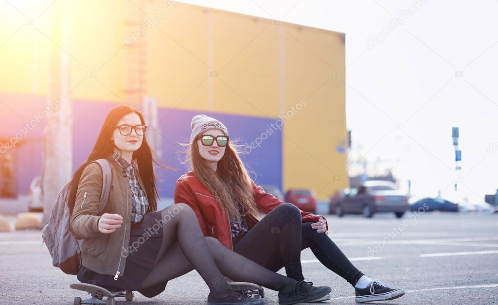 A young hipster girl is riding a skateboard. Girls girlfriends for a walk in city with a skateboard. Spring sports on the street with a skateboard