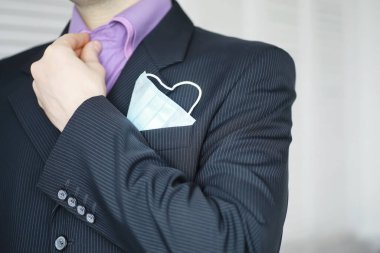 Tek kullanımlık bir tıbbi maske peçeteden sarkıyor. Takım elbiseli ve kot pantolonlu tek kullanımlık maskeli bir adam. Bireysel solunum koruması.