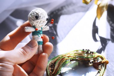 Taştan bir arka planda dramatik ışıklandırmayla vudu bebeği. Büyülü bebeklerle, tarot kartlarıyla, kitaplarla, şeytani mumlarla ve cadılık objeleriyle dolu mistik bir hayat. Kehanet ayini.