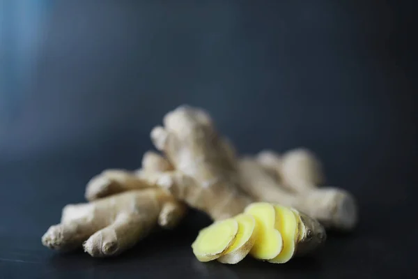 Ginger root whole and sliced. Ginger tea with lemon on the dark background. Fresh ginger root on stone background. Vitamins. Top view. Free space for your text.