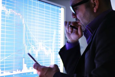 Bir işadamı monitördeki bir grafiğe bakıyor. Borsa simsarı borsa eğilimlerini değerlendirir. Ekonominin dinamiklerinin önünde gözlüklü bir adam..