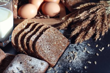 Siyah bir masada buğday ve glüten ile taze somun ekmek. Fırın ve market konsepti. Taze, sağlıklı çavdar ve beyaz somun ekmeği, çuval bezi üzerine serpiştirilmiş un. Tahıllı taze ev yapımı ekmek..