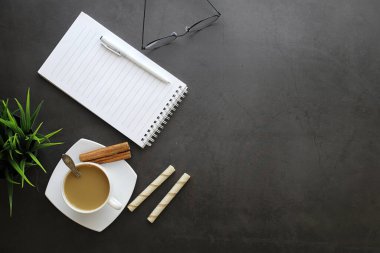 Ofis masaüstü arka planında bir fincan kahve ve yazma aletleri var. Müdürün masası, kalemi, defteri..