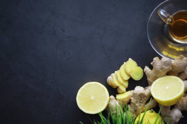 Zencefil kökü bütün ve dilimlenmiş. Koyu arkaplanda limonlu zencefil çayı. Taş zeminde taze zencefil kökü. Vitaminler. Üst Manzara. Metnin için boş yer.