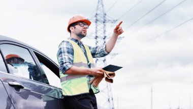 Kasklı ve üniformalı bir adam, sahada bir elektrikçi. Profesyonel elektrik mühendisi elektrik hatlarını inceliyor..