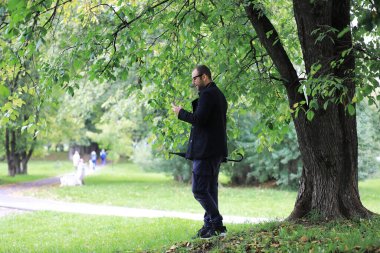 Gözlüklü genç bir adam yağmur sırasında elinde şemsiyeyle parkta yürür..