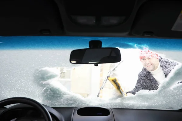 A male driver is standing in front of a car. The owner cleans the car from snow in winter. Car after a snowfall.