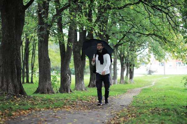 一个戴眼镜的年轻人在下雨时带着雨伞在公园里散步 — 图库照片