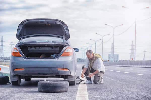 道路上の車のホイールを交換します タイヤの仕事をしてる男が — ストック写真