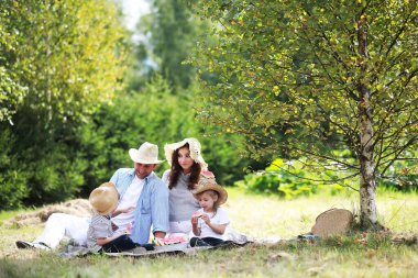 Parkta piknik yapan mutlu bir aile, bahçedeki çimlerde oturan ve dışarıda karpuz yiyen çocukları olan bir aile.