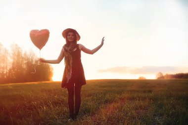 Parkta yürüyüş yapan şapkalı bir kız. Sepetli bir kız sonbaharda yürür. Kız gün batımında yolda yürüyor.