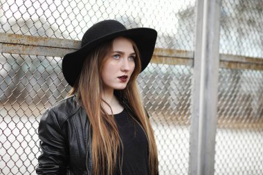 Şapkalı ve dışarıda siyah makyajlı güzel bir kız. Sokakta Gotik tarzında bir kız. Şehir caddesinde bir kız yürüyor. Deri yelekli ve telefonlu.