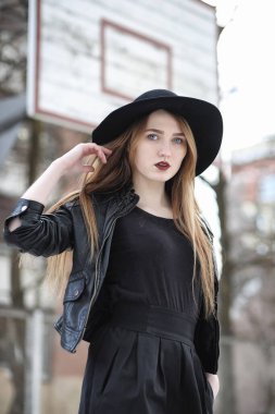 Şapkalı ve dışarıda siyah makyajlı güzel bir kız. Sokakta Gotik tarzında bir kız. Şehir caddesinde bir kız yürüyor. Deri yelekli ve telefonlu.